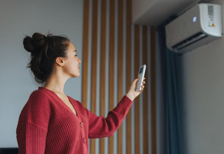 Žena ovládá klimatizaci pro vytápění pomocí mobilního telefonu.