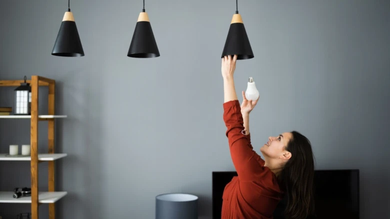 Žena montuje LED žárovku do svítidla.