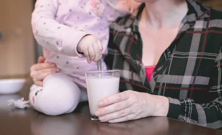 Žena drží sklenici mléka, dítě míchá.
