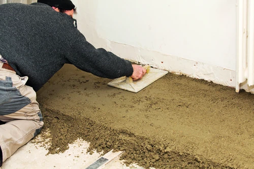 Pracovník roztírá maltu na zemině před pokládkou podlahy.