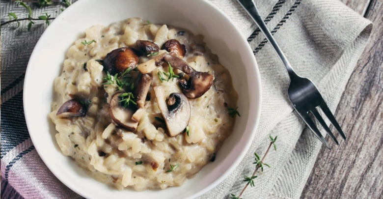 Kremové houbkové risotto v bílé misce s čerstvou bylinkou.