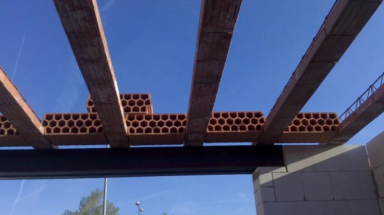 Hurdiskový strop s dřevěnými trámy a betonovými bloky pod modrou oblohou.