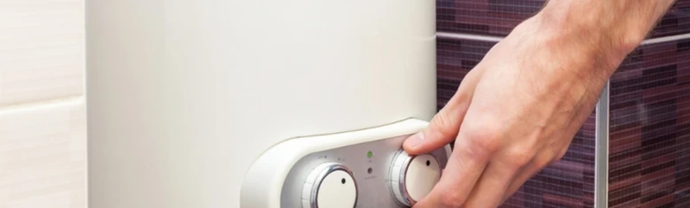 Ruka nastavuje teplotu na elektrickém kotle v koupelně.