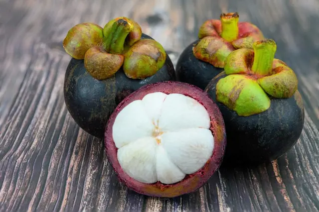 Tři celkové a jeden rozkrojený exotický plod mangostan na dřevě.