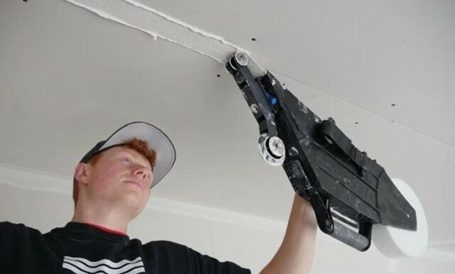 Muž nanáší tmel na spoje sádrokartonu stropu zeď