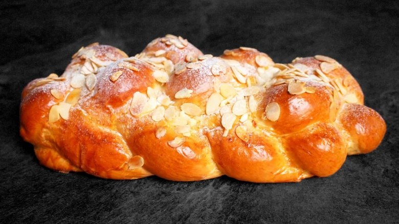 Zlatohnědá vánočka s mandlemi na tmavém pozadí.