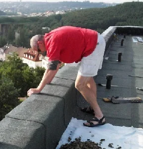 Muž opravuje plochou střechu bez atiky na střeše.