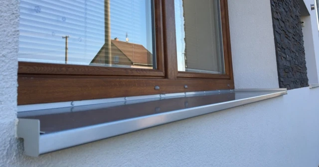 Montovaný venkovní parapet pod oknem s viditelnými držáky.