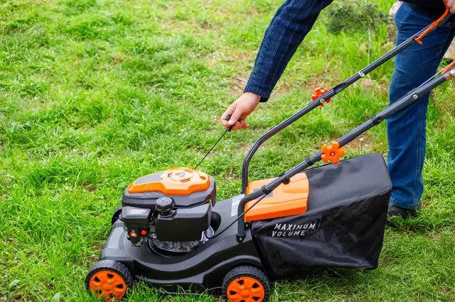 Osoba spouští traktor na sečení trávy v zahradě
