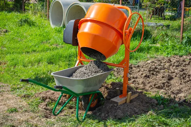 Oranžová betonova míchačka nalévá směs do vozíku.