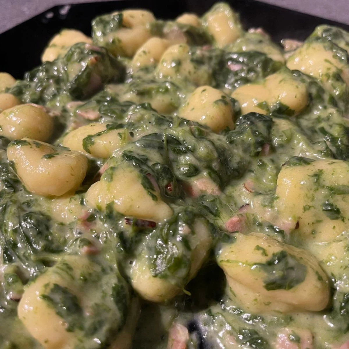 Gnocchi se špenátem, slaninou a smetanou na tmavém talíři