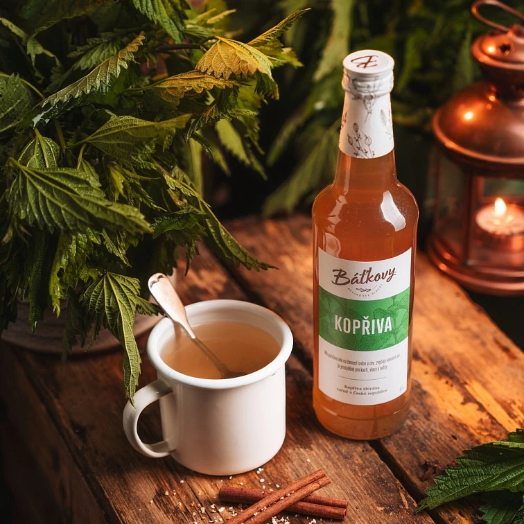 Kopřivový sirup v lahvičce s hrnkem čaje a čerstvou kopřivou