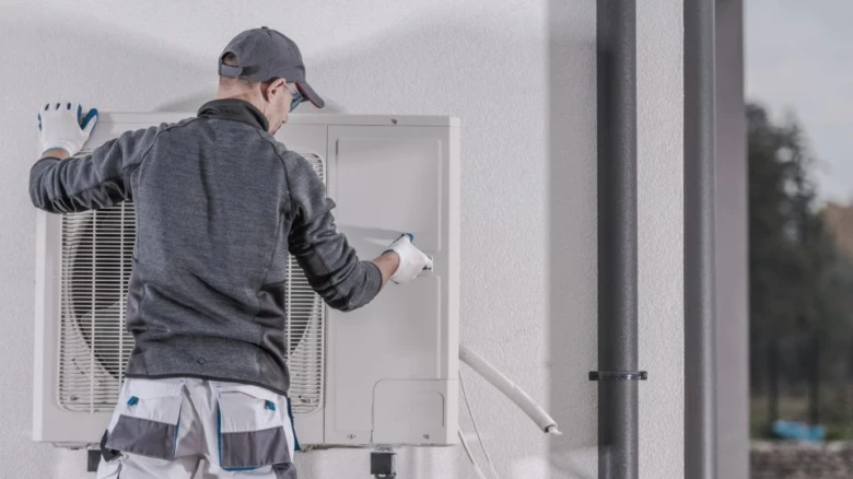 Technik montuje venkovní jednotku tepelného čerpadla na fasádu.
