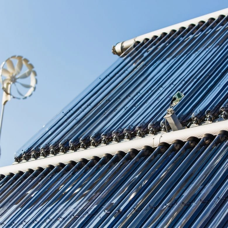 Solární kolektory na střeše s větrným turbínou v pozadí.