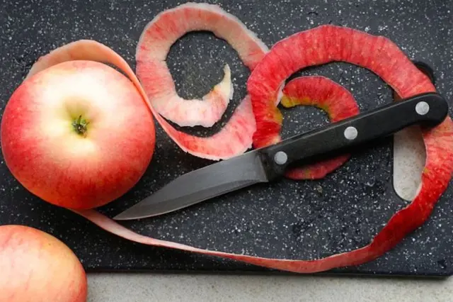 Čerstvé červené jablko s kůrou a nožem na řezacím prkénku.
