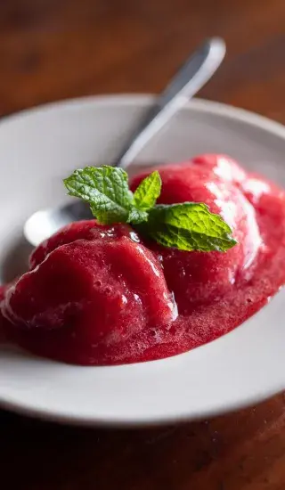 Červený sorbet s mátou na bílém talíři.