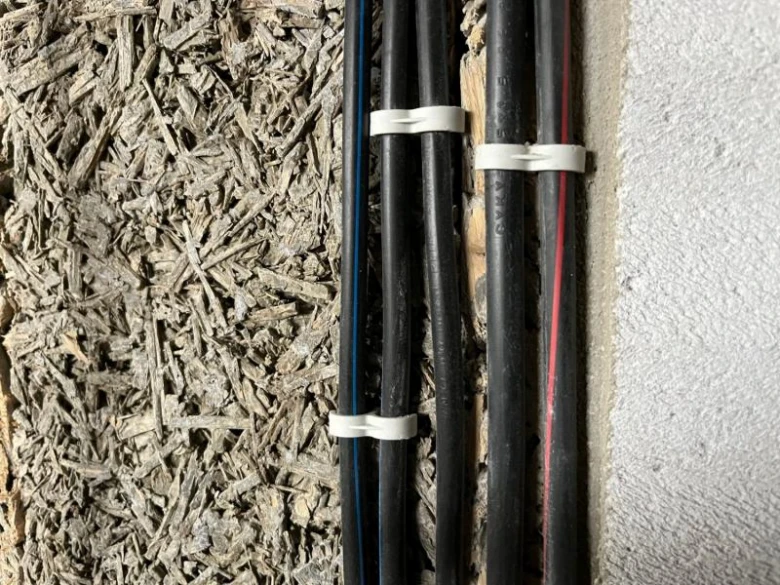 Černé elektrické kabely svázané bílými zip-ties u zdi.