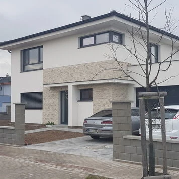 Moderní rodinný dům s kamennou fasádou a parkováním aut.