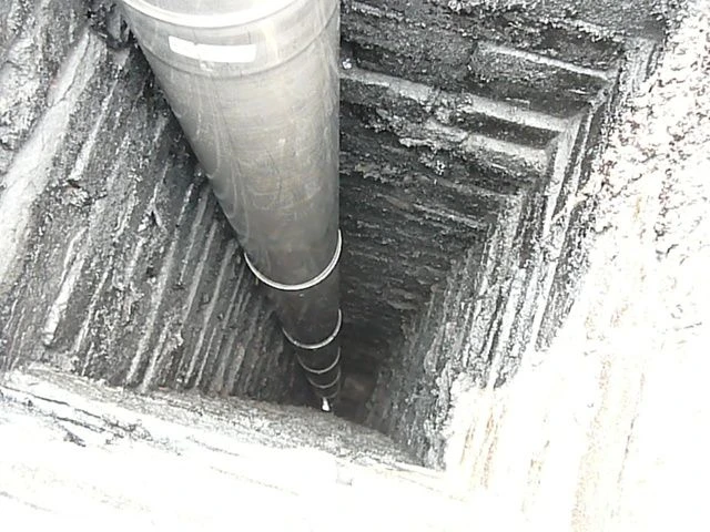Velký kovový potrubí je spouštěno do šachty pro vyvložkování komínu.