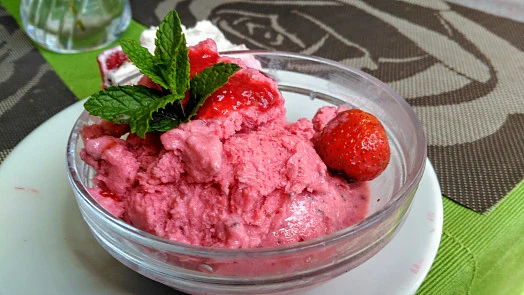 Červený jahodový sorbet v skleněné mísce s mátou.