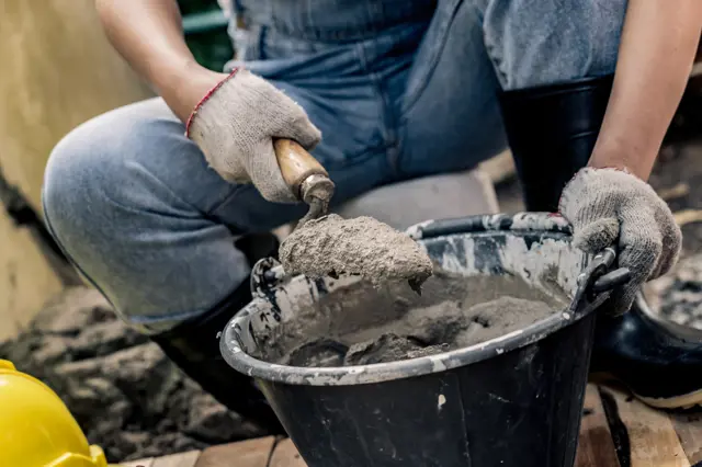 Stavebník míchá beton lopatkou z kbelíku