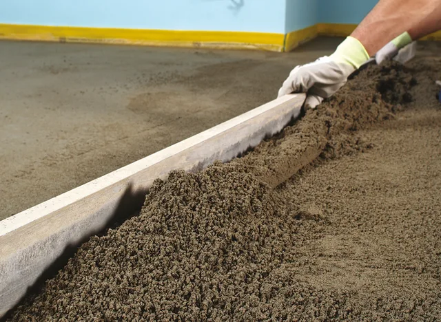 Pracovník vyrovnává čerstvý beton na podlaze pomocí pravítka.