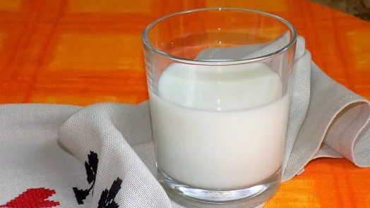 Sklenice bílého mléka na oranžovém podkladu.