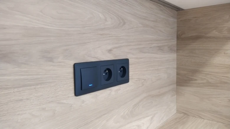 Černý elektrický spínač s zásuvkou na dřevěné stěně.