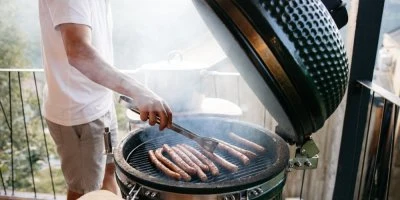 Muž griluje párky na balkóně v zeleném grilu.