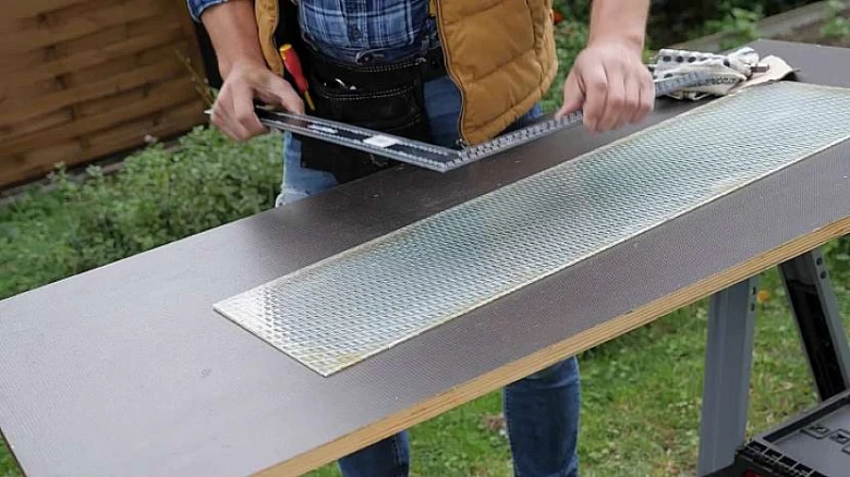 Muž měří kus texturovaného skla na venkovním stole.