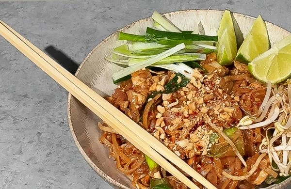 Miska s pad thai špagetami ozdobená citronem a fazolovými klíčky.