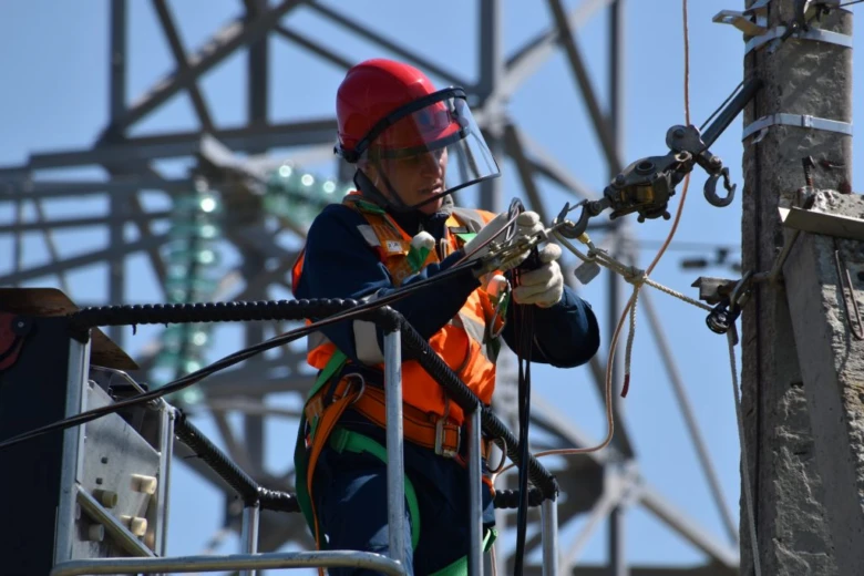 Elektrikář pracuje na vysokonapěťovém vedení u věže.