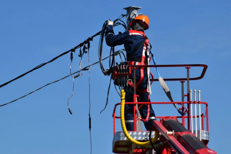 Elektrikář opravuje vedení na výšce v bezpečnostním obleku.